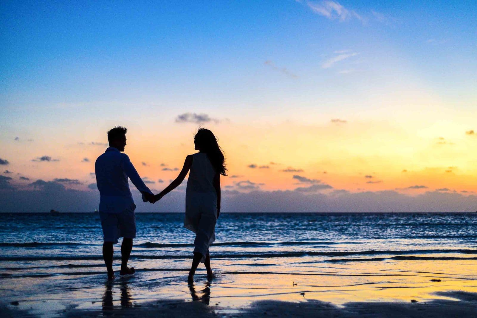 A couple holding hands and walking together along a beach at sunset